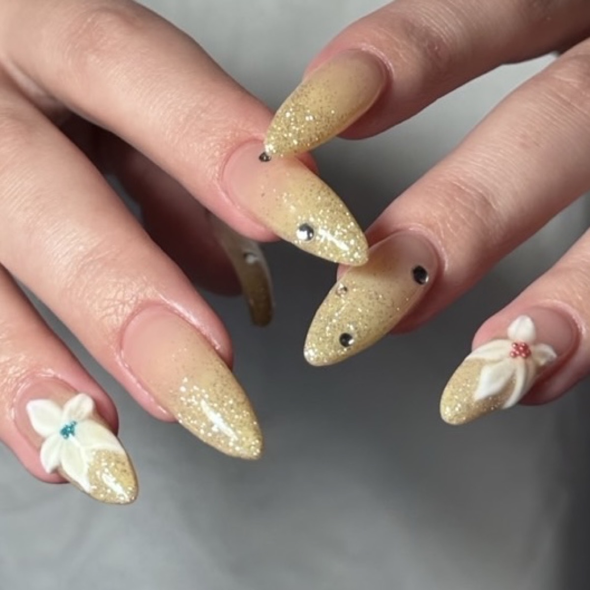Gold glitter nails with white 3D charms at blancher nail salon in Tokyo